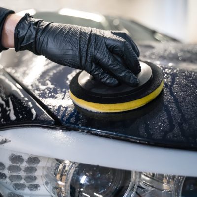 Man cleans car hood with circle sponge. Preparing auto for polishing. 
Detailed car wash